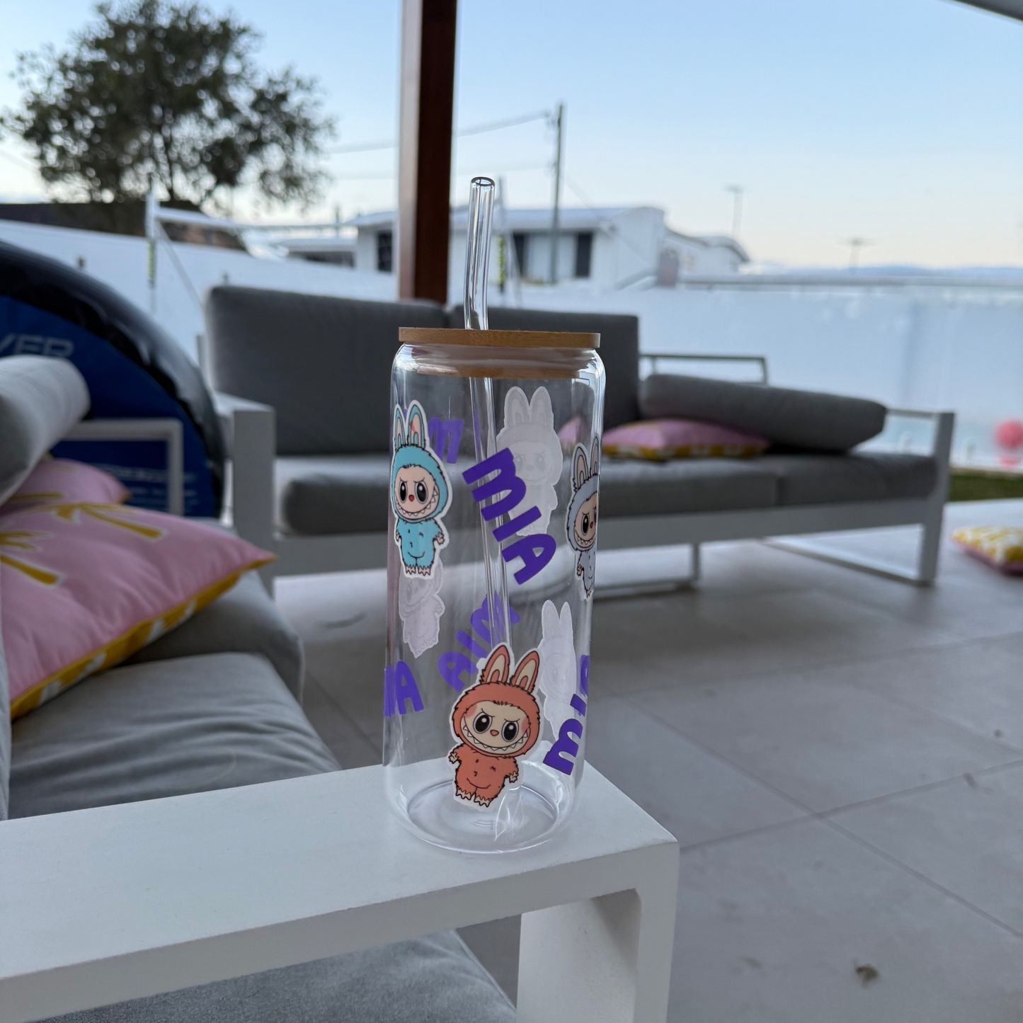 Clear glass tumbler with cartoon characters and text on a white table in an outdoor setting.
