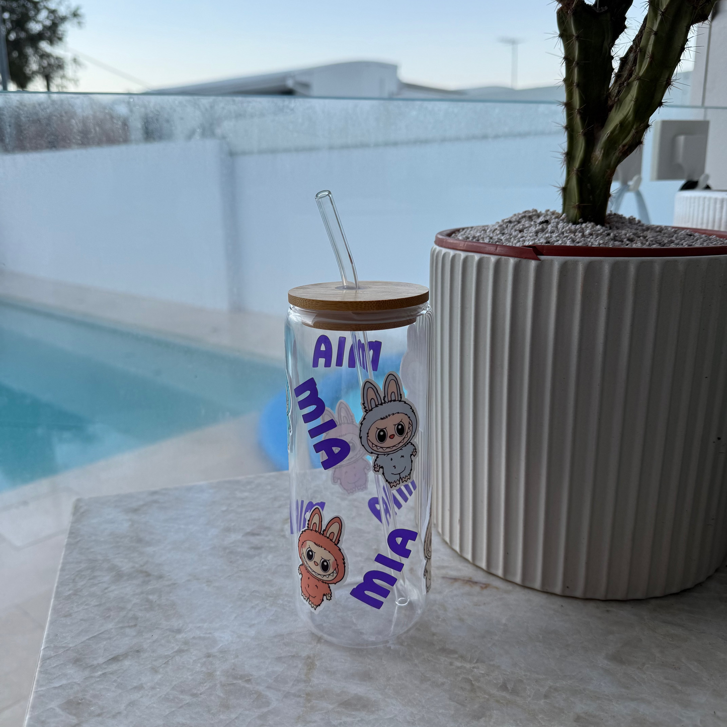 Clear tumbler with cartoon characters and text on a marble surface near a pool.