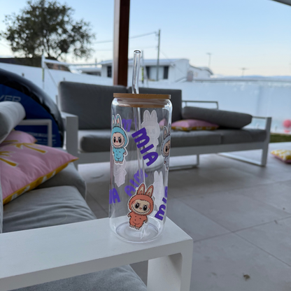 Clear glass tumbler with cartoon characters and text on a white table in an outdoor setting.